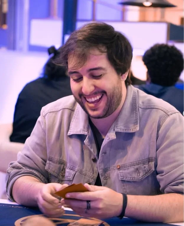 André 'Cast' Bruni segurando cartas Pokémon numa mesa de jogo